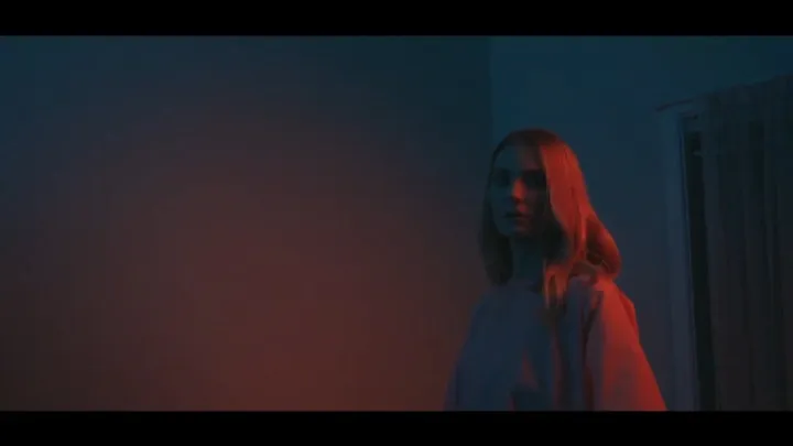 A woman in profile lit with deep red and blue light.