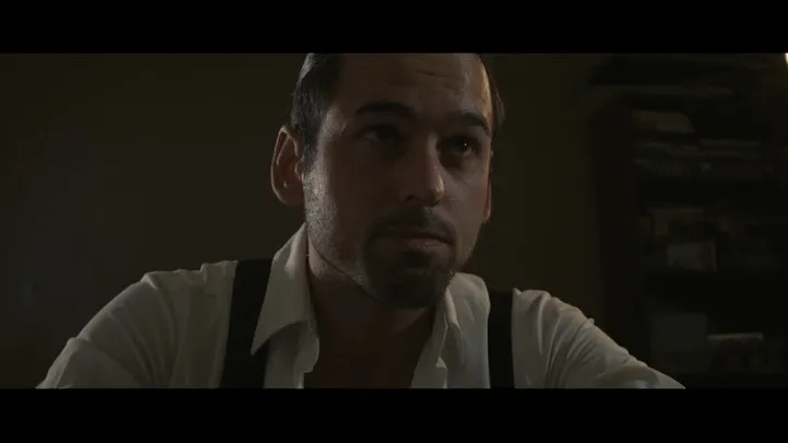 A close portrait of a man emerging from shadow.