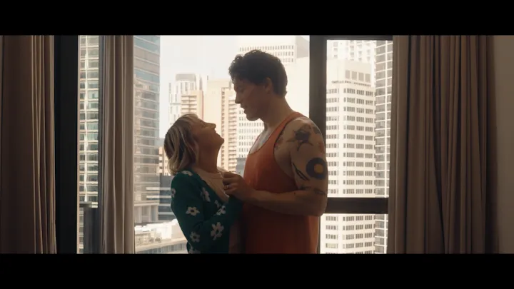 A man and woman talk beside a bright apartment window.