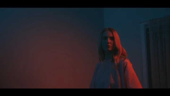 A woman stands in atmospheric red and blue light.