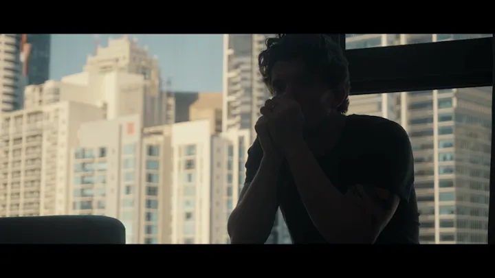 A figure is silhouetted against a city apartment window.