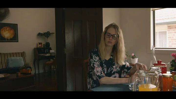 A woman sits at a kitchen table in daylight.