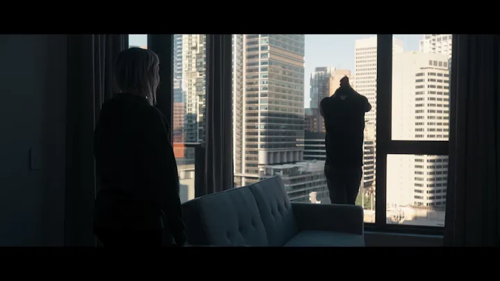 A solitary figure stands at a window above the city.