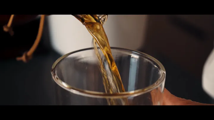 Hands stir coffee in a clear glass.